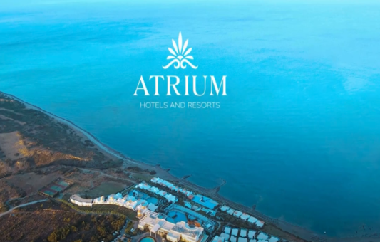 Aerial view of a coastal resort with white buildings near a blue ocean, green landscape on the left, and the Atrium Hotels and Resorts logo centered at the top—perfect for promo videos showcasing luxury stays.